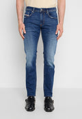 Mann trägt Slim-Fit blaue Denim-Jeans und schwarze Leder Monk-Strap Schuhe, stehend vor einem schlichten hellgrauen Hintergrund.