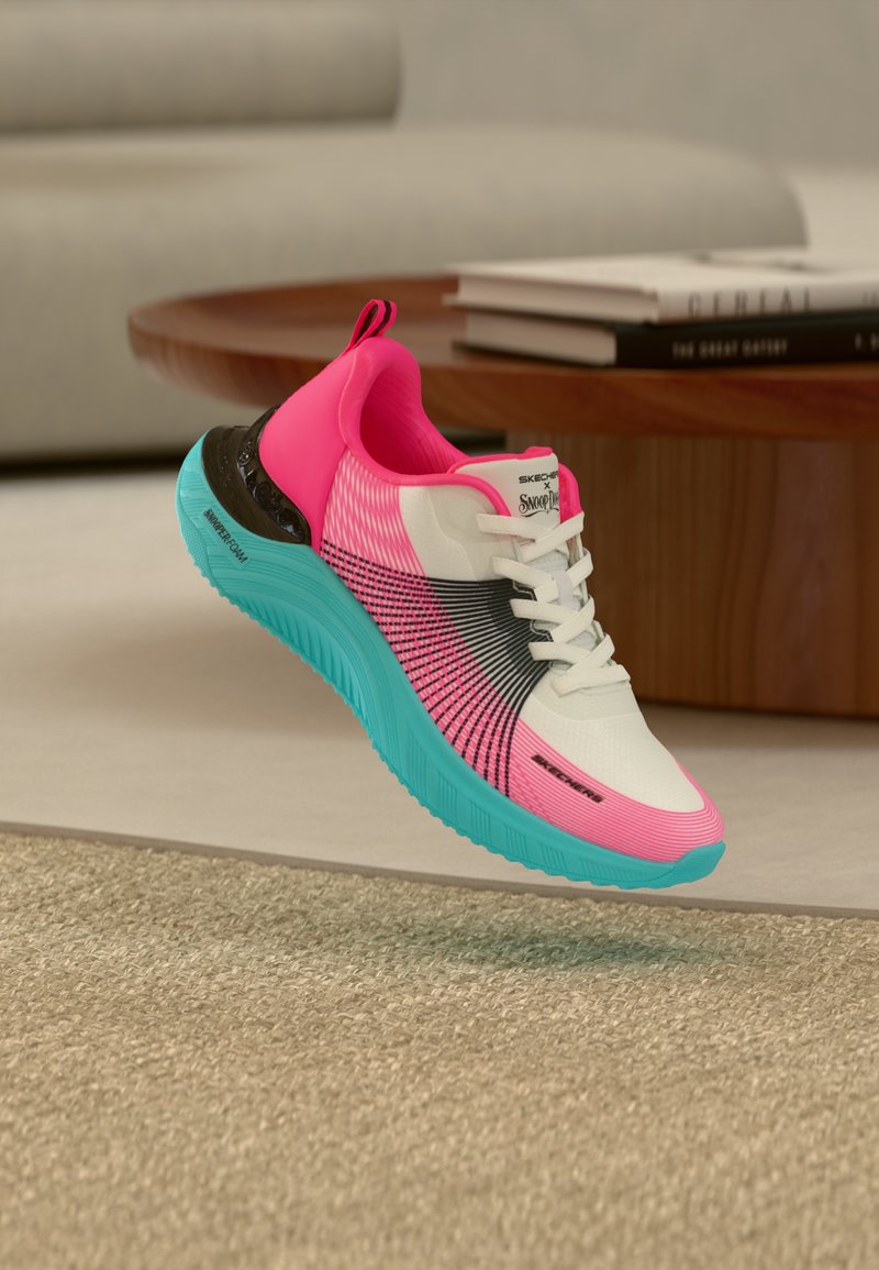 Rosa-weißer und schwarzer Sneaker mit leuchtend blauer Sohle, weißen Schnürsenkeln und "Skechers x Snoop Dogg"-Logo, der über einem beigen Teppich in Innenräumen schwebt.