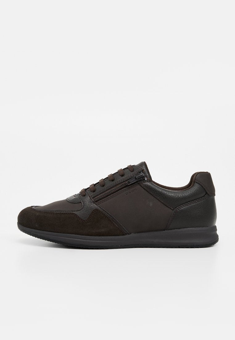 Dunkelbrauner Sneaker mit Schnürung vorne, seitlichem Reißverschluss, gemischten Leder- und Veloursleder-Paneelen und einer schwarzen Gummisohle, von der linken Seite gezeigt.