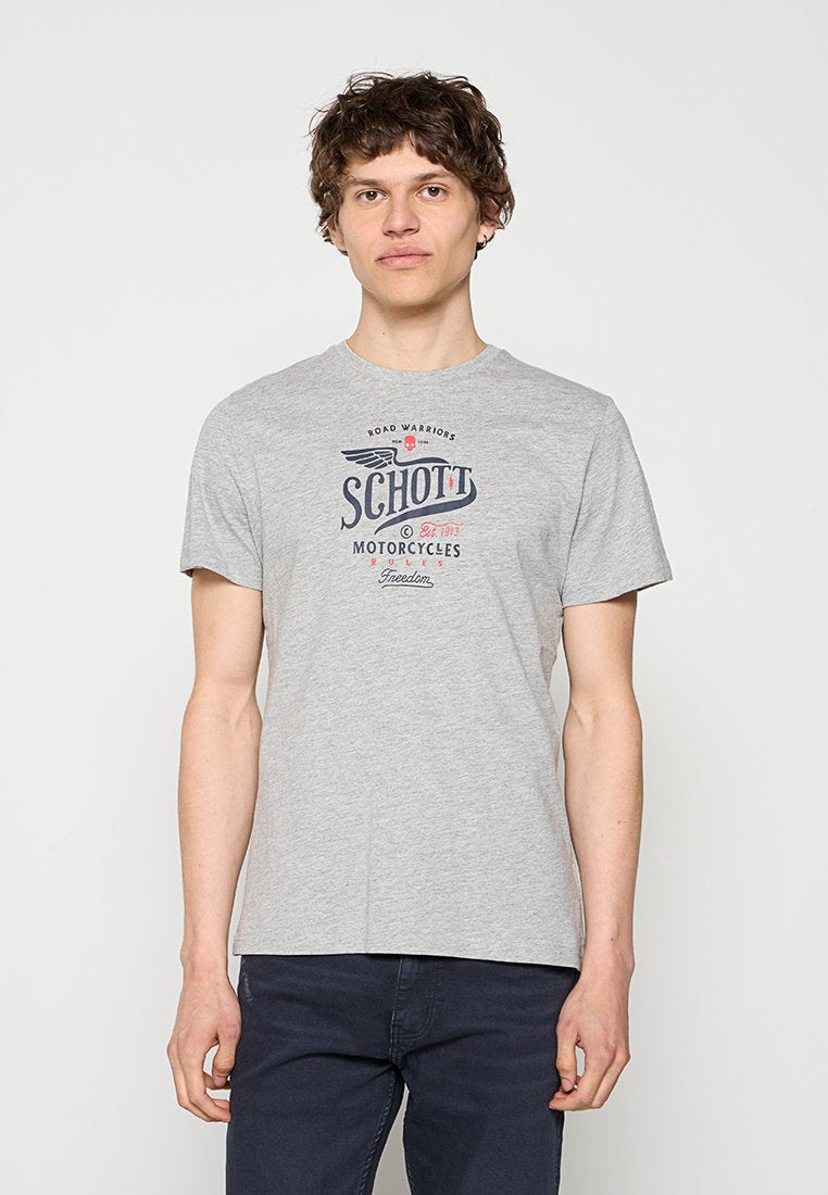 Junger Mann mit lockigem Haar, der ein graues "Schott Motorcycles" T-Shirt und dunkle Hosen trägt, steht vor einem schlichten weißen Hintergrund.
