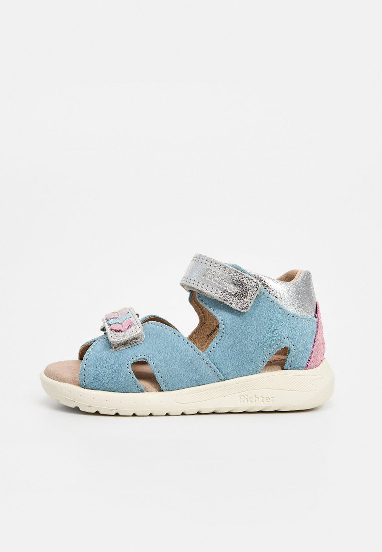 Hellblaue Kleinkind-Sandale mit pinkfarbenem Fersenpatch, silberfarbenem Metallic-Knöchelriemen und weißer Sohle, ausgestattet mit zwei verstellbaren Klettverschlüssen.