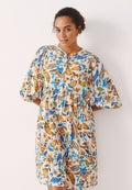 Blumenkleid aus weißem Stoff mit bunten Mustern von orangefarbenen, blauen und grünen Blättern; kurze Puffärmel und Knopfverschluss vorne.