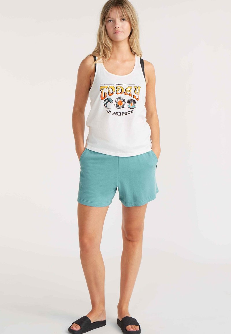 Weißes Tanktop mit grafischem Text und Mustern, kombiniert mit türkisfarbenen Shorts. Die Shorts haben seitliche Taschen und einen entspannten Schnitt und werden mit schwarzen Schippersandalen getragen.
