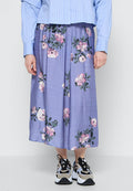 Blumen-Midi-Rock aus leicht lila Stoff mit pinken und weißen Blumenmustern, kombiniert mit schwarz-weißen Sneakers.