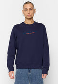 Person in einem marineblauen Rundhalsausschnitt-Sweatshirt mit dem Schriftzug "Diesel Industry Denim Division", kombiniert mit lockeren blauen Jeans, steht vor einem weißen Hintergrund.