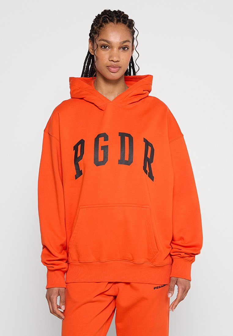 Orangene Kapuzenjacke mit schwarzer "PGDR" Schriftzug, lässiger Schnitt, Vordertasche und gerippten Bündchen und Saum. Weicher Stoff.