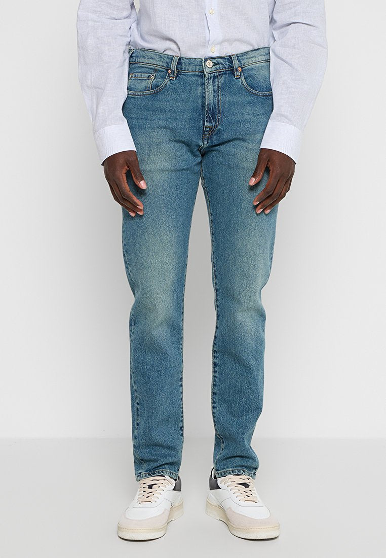 Hellblaue Jeans im Slim-Fit mit einer verwaschenen Optik, fünf Taschen und klassischem Knopfverschluss. Kombiniert mit weißen Sneakers.
