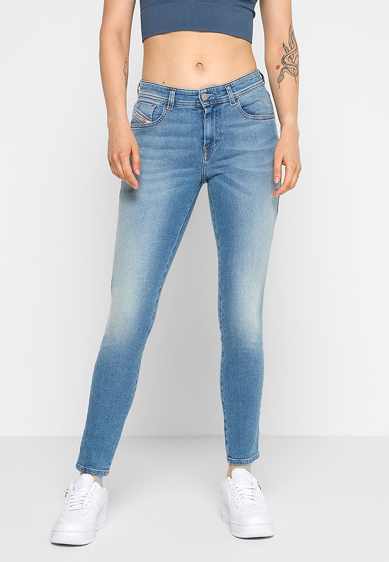 Hellblaue Skinny Jeans mit einem verblassten Effekt, Fünf-Taschen-Design und Knopfverschluss. Kombiniert mit einem grauen Cropped-Top und weißen Sneakers.