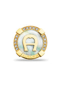 Goldfarbener, runder Anstecker mit einem zentralen, hellen Stein und einem 'A'-Logo, umgeben von kleinen, klaren Kristallen und akzentuiert mit goldfarbenen Beschlägen.