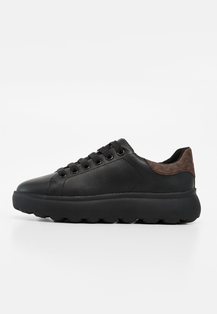Schwarzer Low-Top-Sneaker mit dicker Sohle, schwarzen Schnürsenkeln und braunem strukturiertem Fersenpatch, von der Außenseite auf weißem Hintergrund gezeigt.