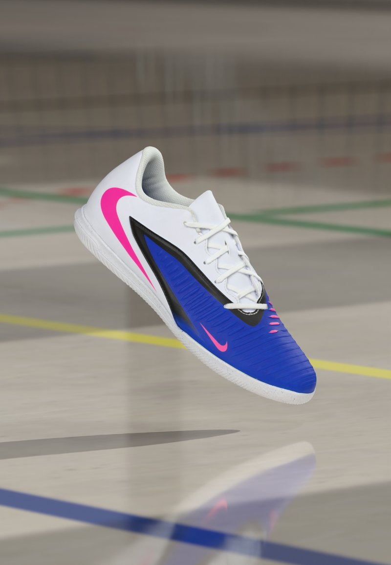 Nike Sportschuh mit blauem Obermaterial und strukturiertem Design, weißen Akzenten, pinkem Logo und schwarzen Details, für den Innenbereich entwickelt.