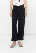 Schwarze Schlagjeans aus Denim-Material, mit hohem Bund, fünf Taschen und subtiler tonaler Steppnaht. Kombiniert mit minimalistischen Riemchensandalen.