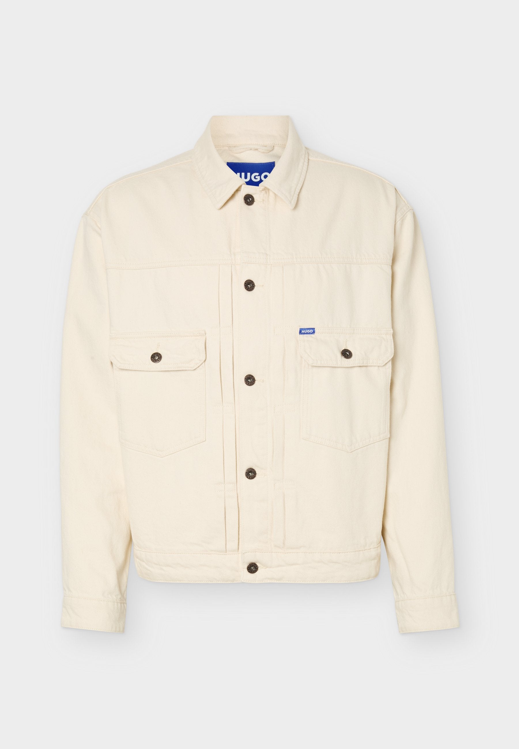 Beige Jacke mit langen Ärmeln, Knopfleiste, zwei Brustklappentaschen, einem Kragen und einem kleinen blauen Logoschild an der rechten Tasche.