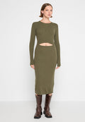 Olivgrünes, geripptes Langarmkleid mit einem Ausschnitt in Taillenhöhe. Figurbetonte Silhouette, knielang, kombiniert mit braunen kniehohen Stiefeln. Glatte Textur.
