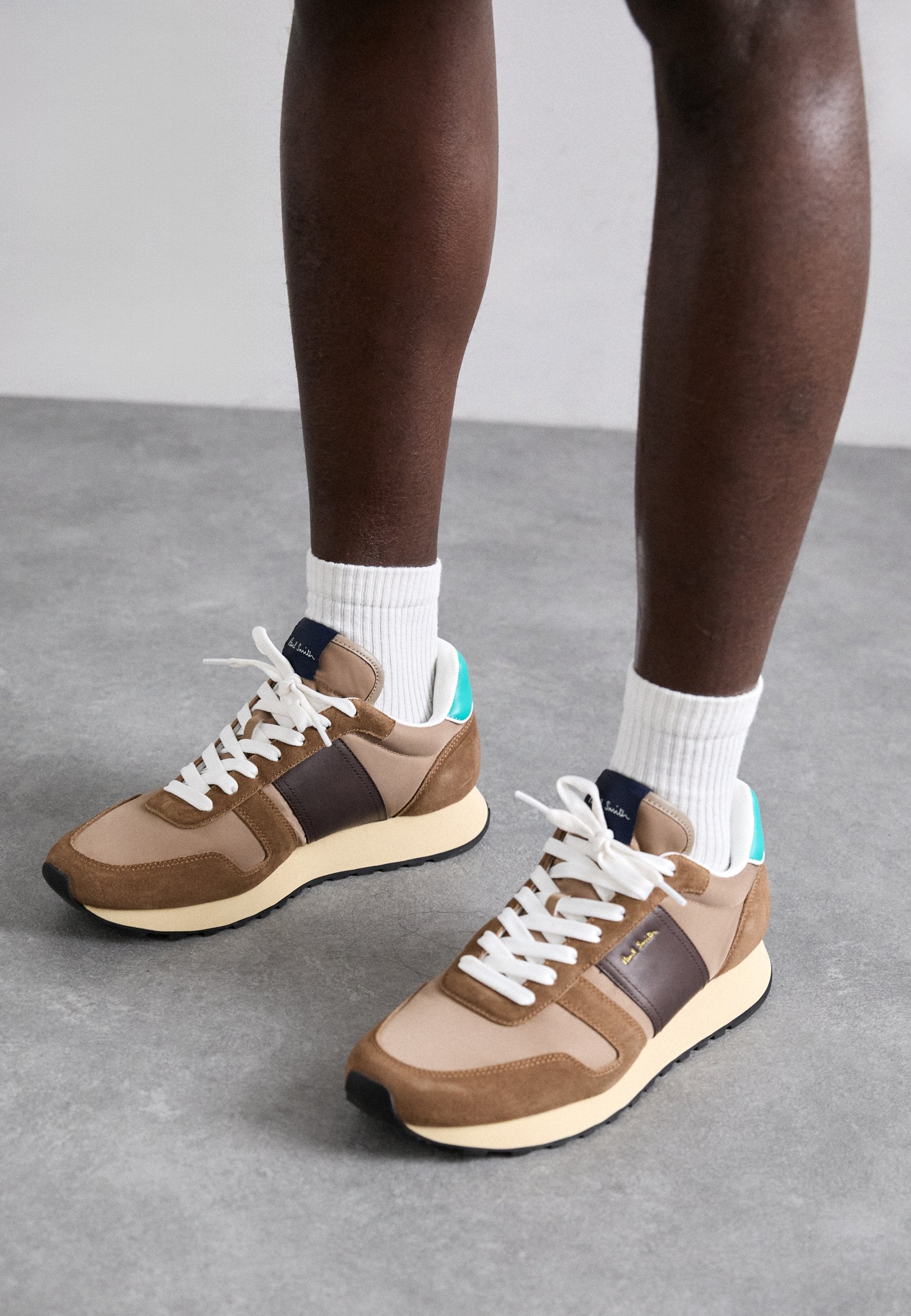 Braune und beige Sneaker mit weißen Schnürsenkeln, aus Leder und Wildleder, einem türkisfarbenen Akzent an der Ferse und einer cremefarbenen Gummisohle.