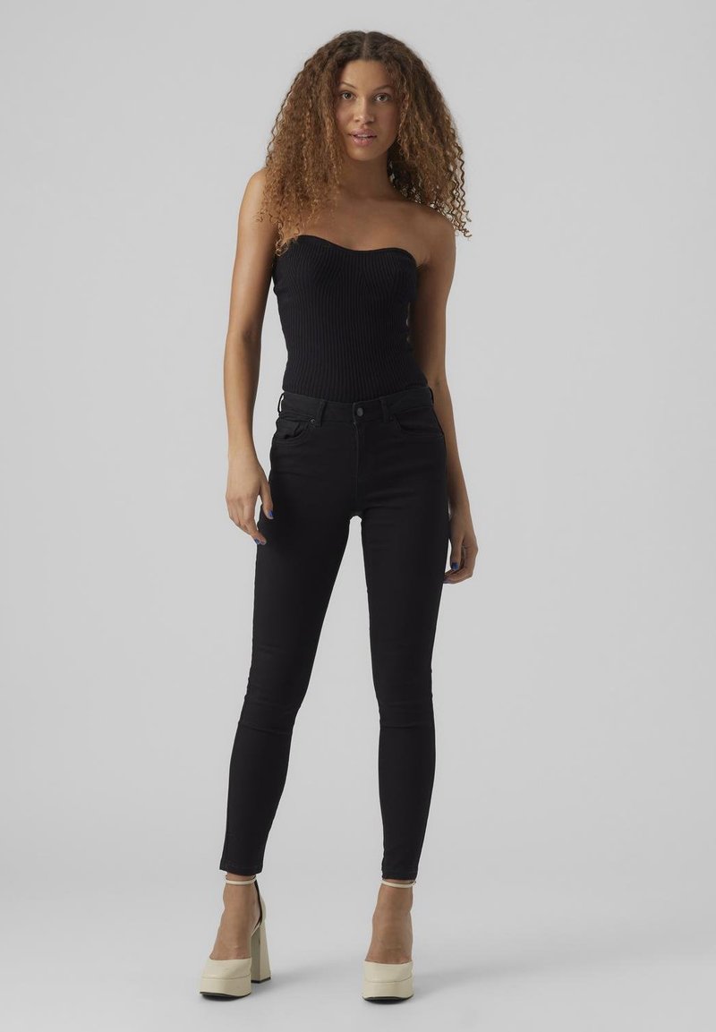 Schwarzes, geripptes, trägerloses Oberteil kombiniert mit enganliegenden schwarzen Jeans und cremefarbenen High-Heel-Plateauschuhe. Glatte Textur, eleganter Schnitt.