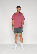 Herren-T-Shirt mit kurzen Ärmeln in Kastanienbraun von Nike, kombiniert mit dunkelgrauen, strukturierten Shorts mit Logo-Patch, weißen Socken und weißen Turnschuhen.