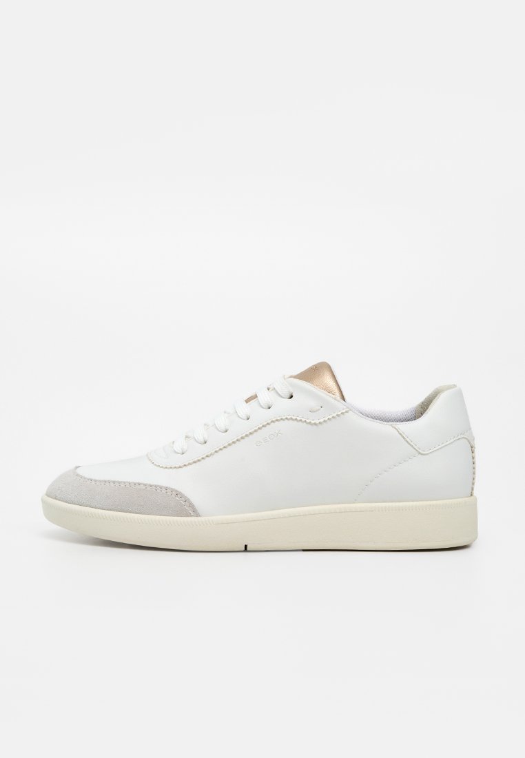 Weißer Sneaker mit niedrigem Schaft, beiger Zehenkappe, cremefarbiger Sohle und metallischem goldfarbenem Zungendetail, seitlich auf weißem Hintergrund dargestellt.