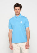 Mann steht vor einem schlichten Hintergrund, trägt ein hellblaues Poloshirt mit weißem Besatz und Vogel-Logo sowie cremefarbene Hosen.