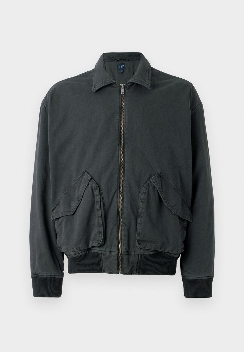 Schwarze Bomberjacke mit Reißverschluss, zwei großen Seitentaschen, gerippten Bündchen und Kragen. Aus strapazierfähigem Stoff mit glatter Textur gefertigt.