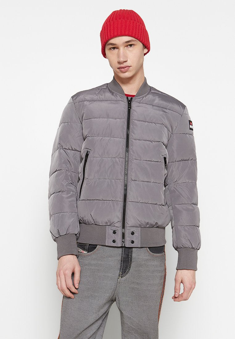 Graue Pufferjacke mit einem Reißverschluss vorne und gerippten Bündchen, mit horizontalen Steppnähten und zwei vorderen Taschen. Rote Strickmütze.