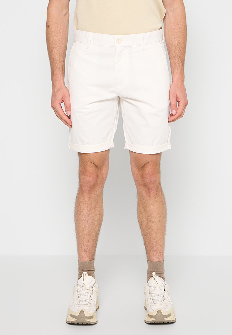 Weiße Baumwollshorts, enganliegendes Design, umgeschlagener Saum, vorderer Knopfverschluss, Seitentaschen, kombiniert mit beigen Turnschuhen und taupefarbenen Socken.