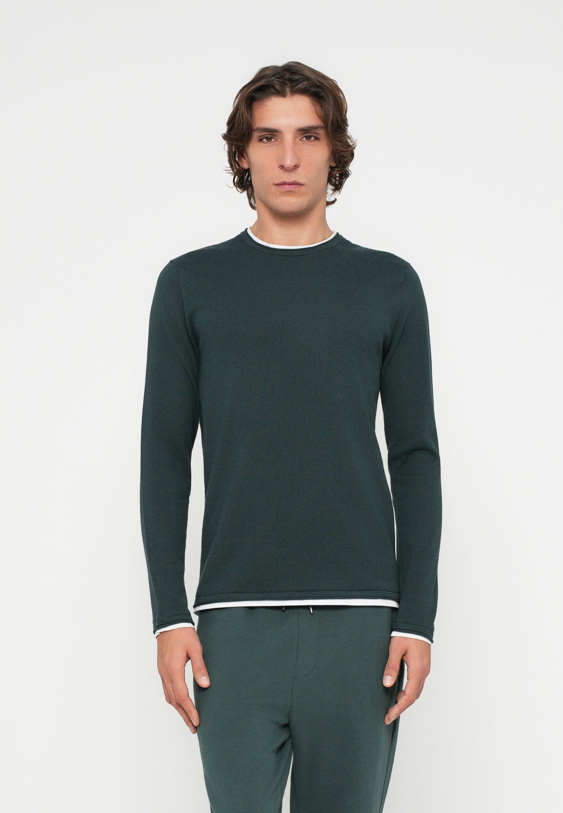 Dunkelgrünes Langarmshirt mit rundem Ausschnitt, versehen mit weißem Besatz am Kragen und an den Manschetten, gefertigt aus einem strukturierten Stoff.