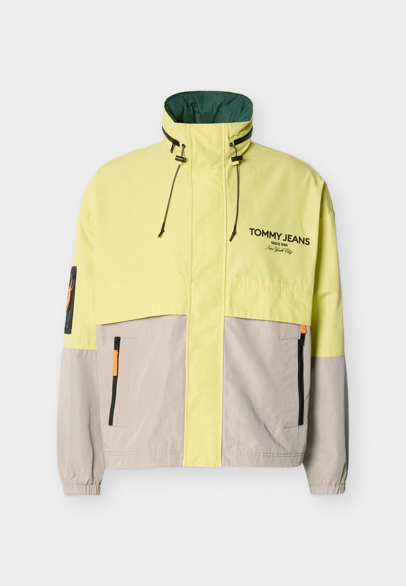 Halb gelbe, halb graue Jacke mit Reißverschluss, hohem Kragen, verstellbaren Kordeln, elastischen Bündchen, Seitentaschen und "Tommy Jeans"-Logo auf der Brust.