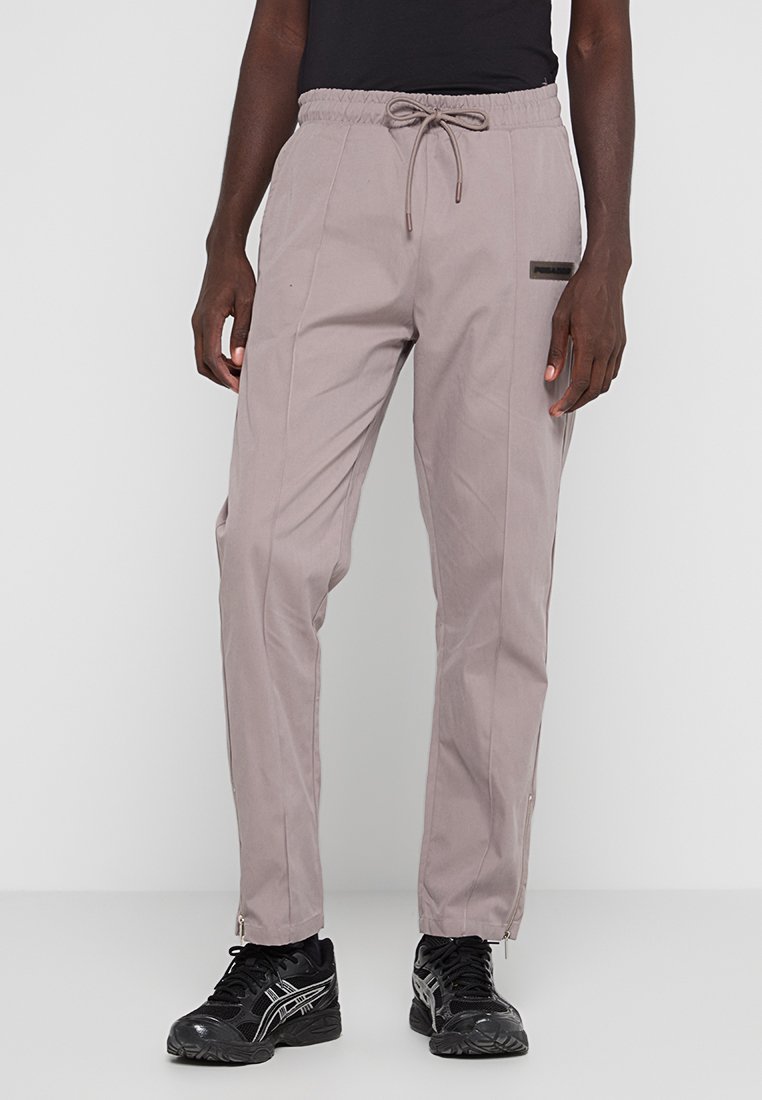 Helle graue Hose aus gewebtem Stoff, mit einem elastischen Bund und einem Kordelzug, seitlichen Taschen und Reißverschlüssen an den Knöcheln.
