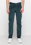 Tealfarbene Cordhose mit geradem Bein, ausgestattet mit Reißverschluss, fünf Taschen und subtiler Textur. Kombiniert mit weißen Turnschuhen.