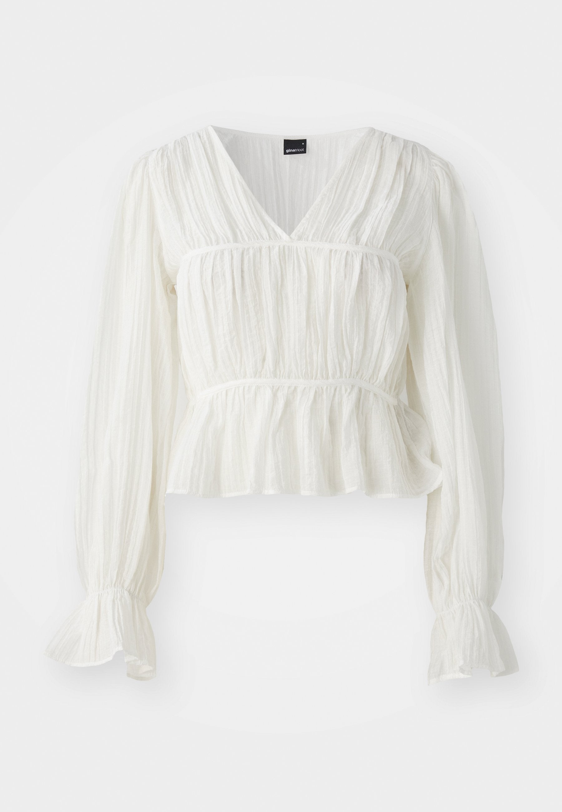 Weiße Bluse mit langen Ärmeln und V-Ausschnitt, strukturiertem Stoff, gerafftem Oberteil und einem Peplum-Saum. Ausgestellte Manschetten bieten zusätzliche Details.