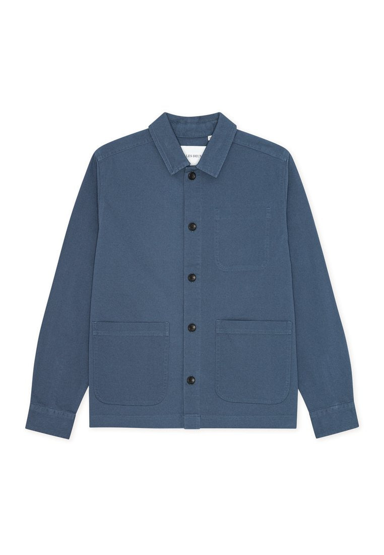 Blaue Baumwolljacke mit Kragen, durchgehender Knopfleiste, zwei großen aufgesetzten Taschen und einer einzelnen Brusttasche. Glatte Textur.