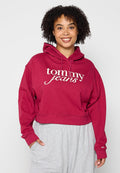 Burgunderrotes Cropped Hoodie mit weißem "Tommy Jeans" Logo, Kapuze mit Zugband und lockerer Passform. Kombiniert mit hellgrauen Sweatpants.