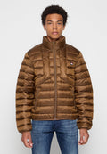 Braune Puffjacke mit hohem Kragen, gestepptem Design, Reißverschluss und Logo-Patch auf der Brust. Getragen über blauen Jeans.