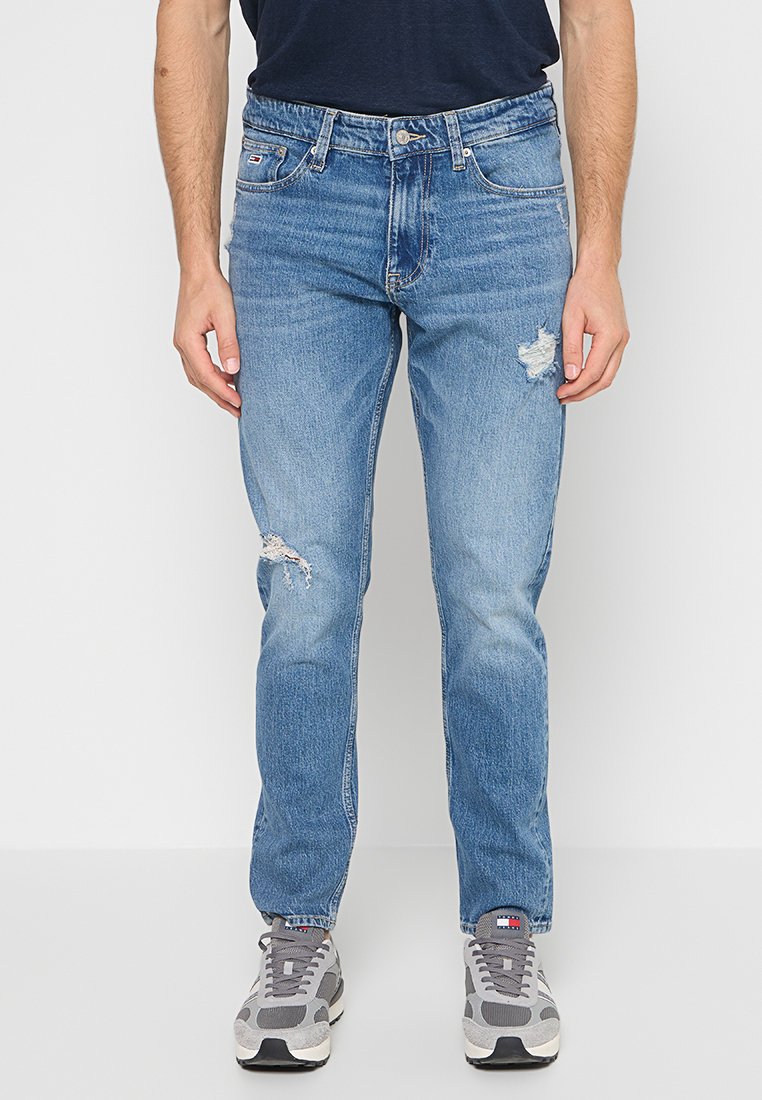 Hellblaue Denim-Jeans mit Slim Fit und distressed Details. Kombiniert mit grauen Sneakers. Klassischer flacher Bund und Fünf-Taschen-Design.