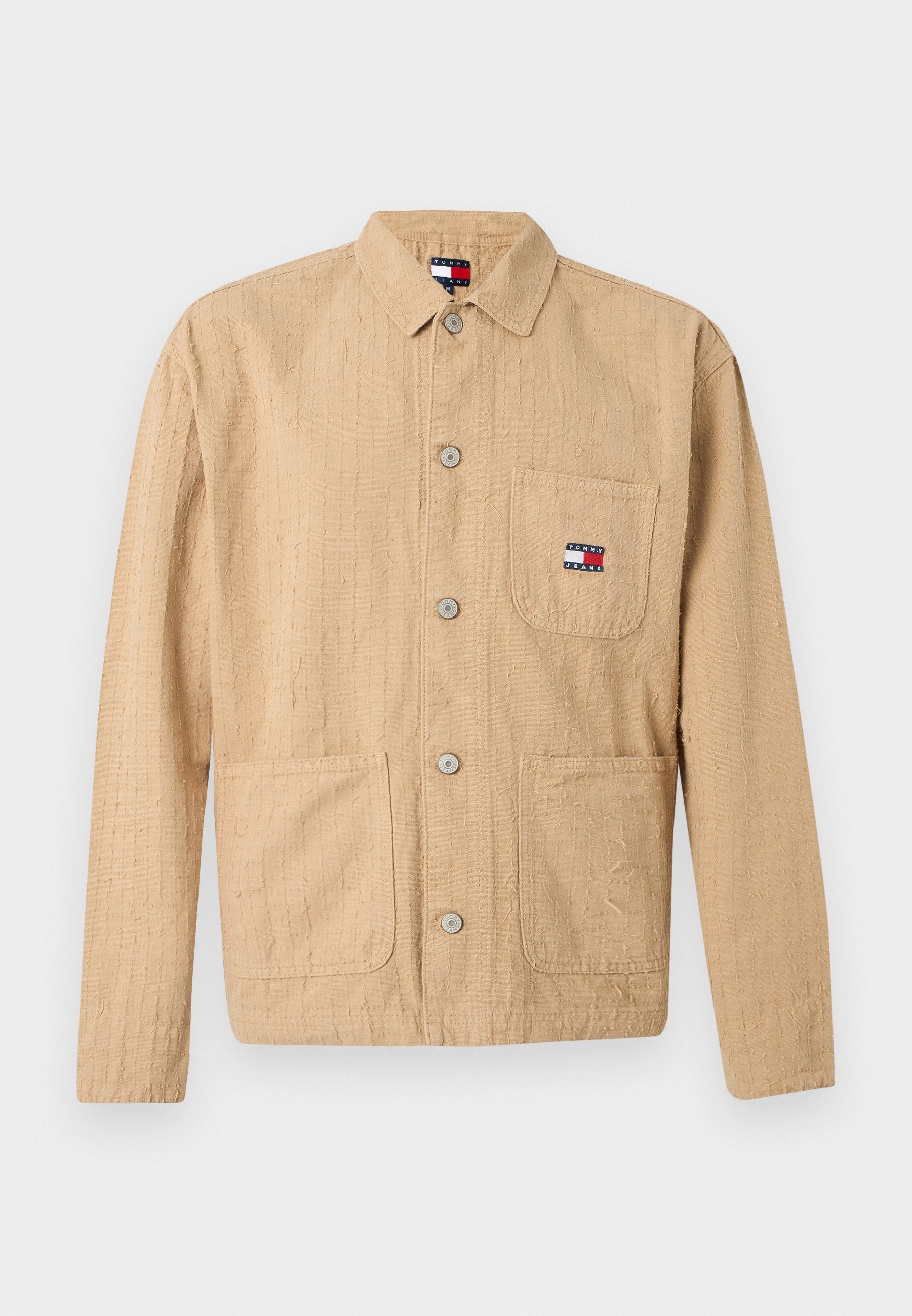 Beige texturierte Jacke mit langen Ärmeln, Knopfleiste, drei Taschen und kleinem Tommy Jeans-Logo auf der Brusttasche sowie am Kragenetikett.