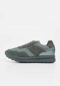 Grauer Sneaker mit Mesh- und Wildleder-Paneelen, Schnürverschluss, gepolstertem Kragen und dicker Gummisohle, seitlich auf weißem Hintergrund dargestellt.