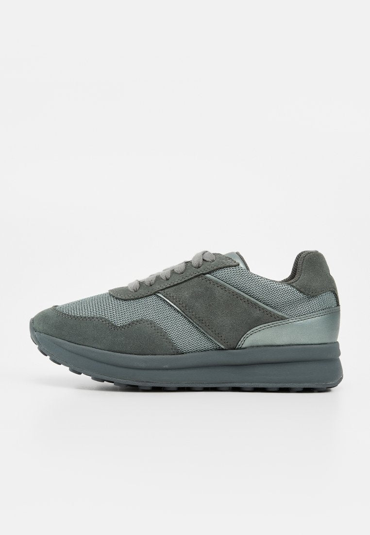 Grauer Sneaker mit Mesh- und Wildleder-Paneelen, Schnürverschluss, gepolstertem Kragen und dicker Gummisohle, seitlich auf weißem Hintergrund dargestellt.