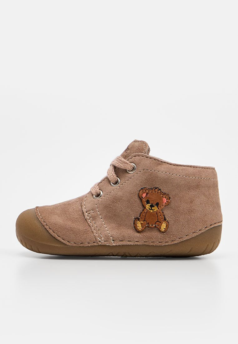 Brauner Wildleder-Kinderschuh mit Schnürsenkeln und Gummisohle, mit einem aufgenähten Teddybär-Aufnäher an der Seite.
