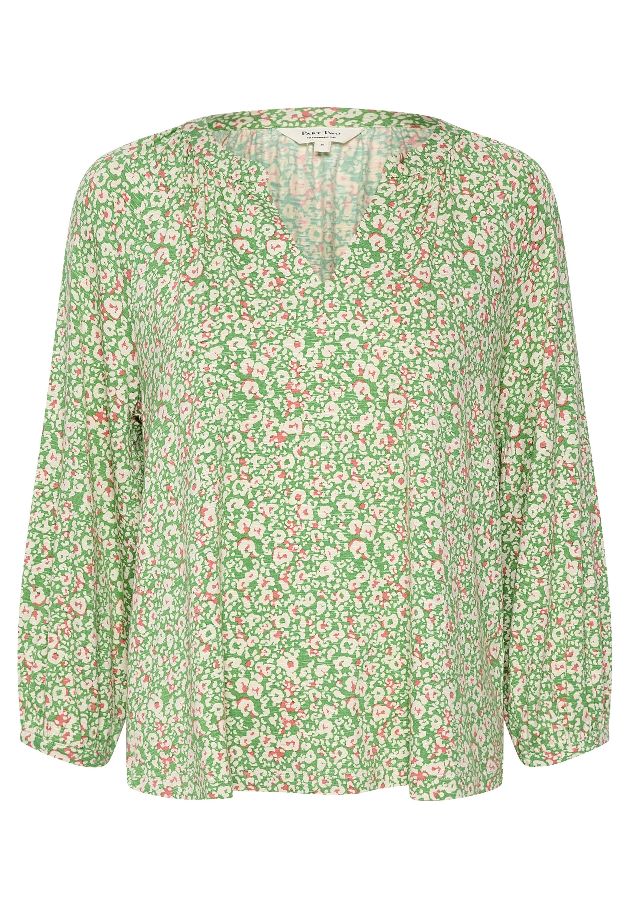 Grünblümige Bluse mit langen Ärmeln und V-Ausschnitt. Das Stoffmuster zeigt rosa und weiße Blumen auf einem strukturierten Hintergrund.