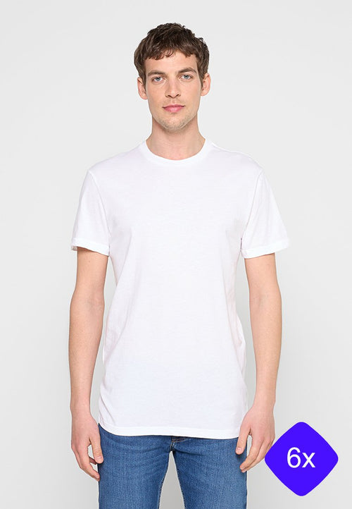 Junger Mann trägt ein schlichtes weißes Kurzarm-T-Shirt und blaue Jeans, steht vor einem neutralen hellen Hintergrund.