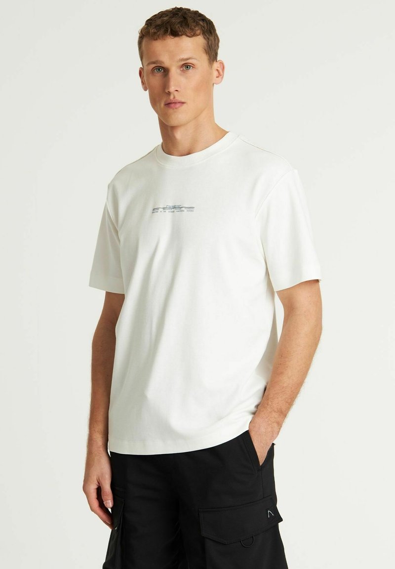 Weißes T-Shirt mit Rundhalsausschnitt, aus Baumwolle und mit kurzen Ärmeln. Besitzt einen subtilen grafischen Druck in Blau auf der Brust. Schlicht und lässig geschnitten.