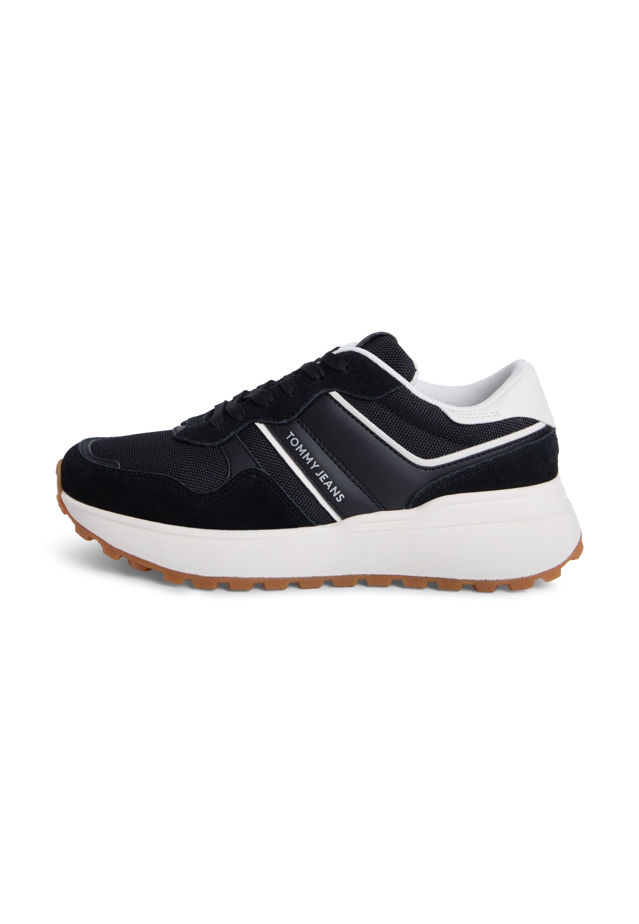Schwarze und marineblaue Turnschuhe aus Mesh- und Wildledermaterialien, mit einer dicken weißen Sohle und einem weißen Akzentstreifen mit der Aufschrift "TOMMY JEANS".