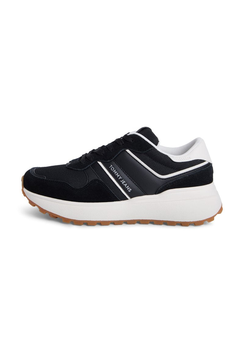 Schwarze und marineblaue Turnschuhe aus Mesh- und Wildledermaterialien, mit einer dicken weißen Sohle und einem weißen Akzentstreifen mit der Aufschrift "TOMMY JEANS".