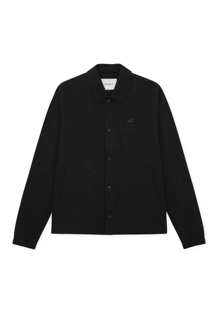 Schwarze Jacke mit Knopfleiste, Kragen, zwei Seitentaschen, elastischen Bündchen und einem dezenten Logodetail auf der Brust. Hergestellt aus einem glatten Stoff.