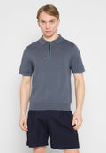 Graues kurzärmeliges Poloshirt mit Reißverschluss am Ausschnitt und farbenfrohen Details. Gerippte Textur und figurbetonter Saum. Getragen zu navyblauen Shorts.