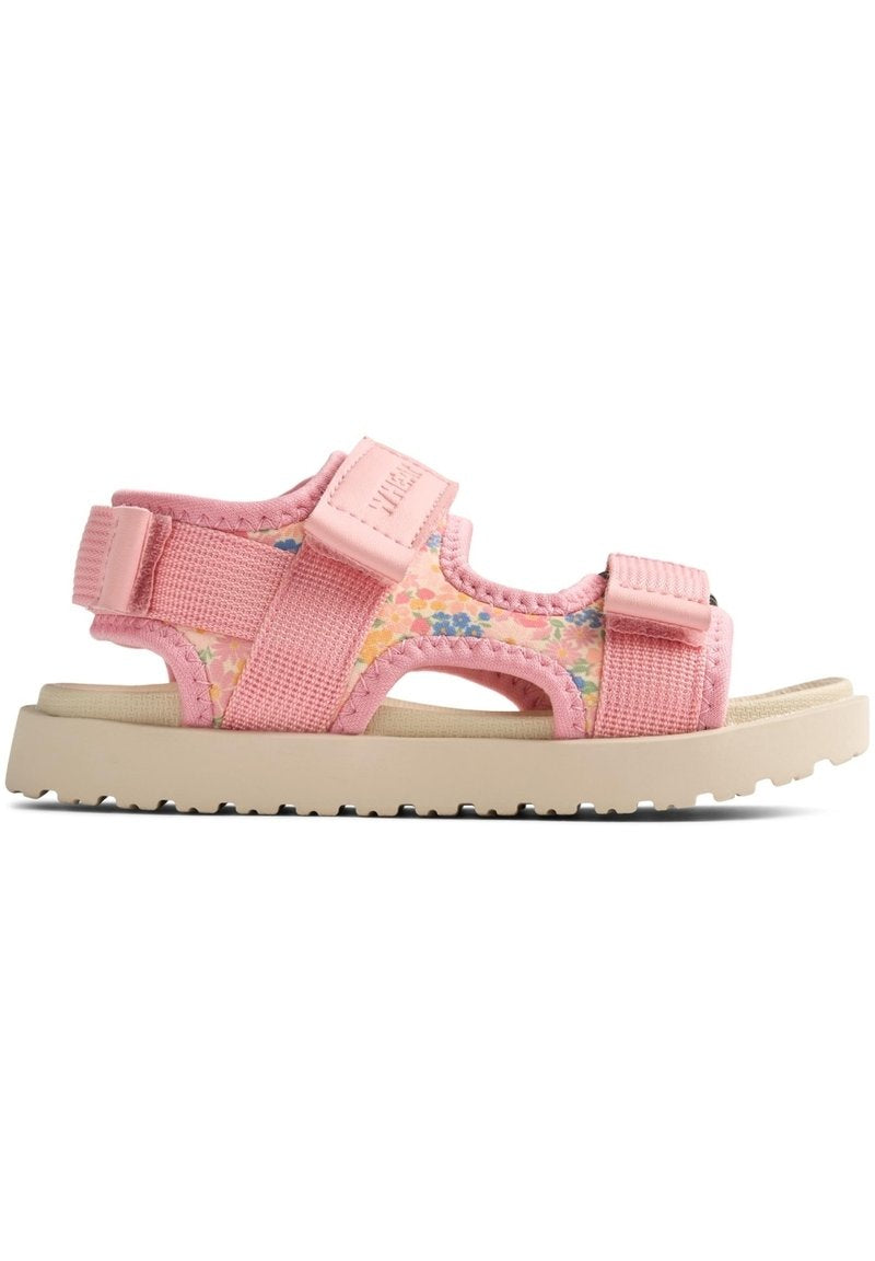 Rosa Kinder-Sandalen mit einem Obermaterial aus floral gemustertem Stoff, verstellbaren Riemen und einer beigefarbenen Gummisohle mit strukturiertem Profil.