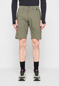 Mann trägt olivgrüne knielange Shorts, schwarzes Langarmshirt, schwarze Socken und mehrfarbige Sportschuhe und steht vor einfachem Hintergrund.