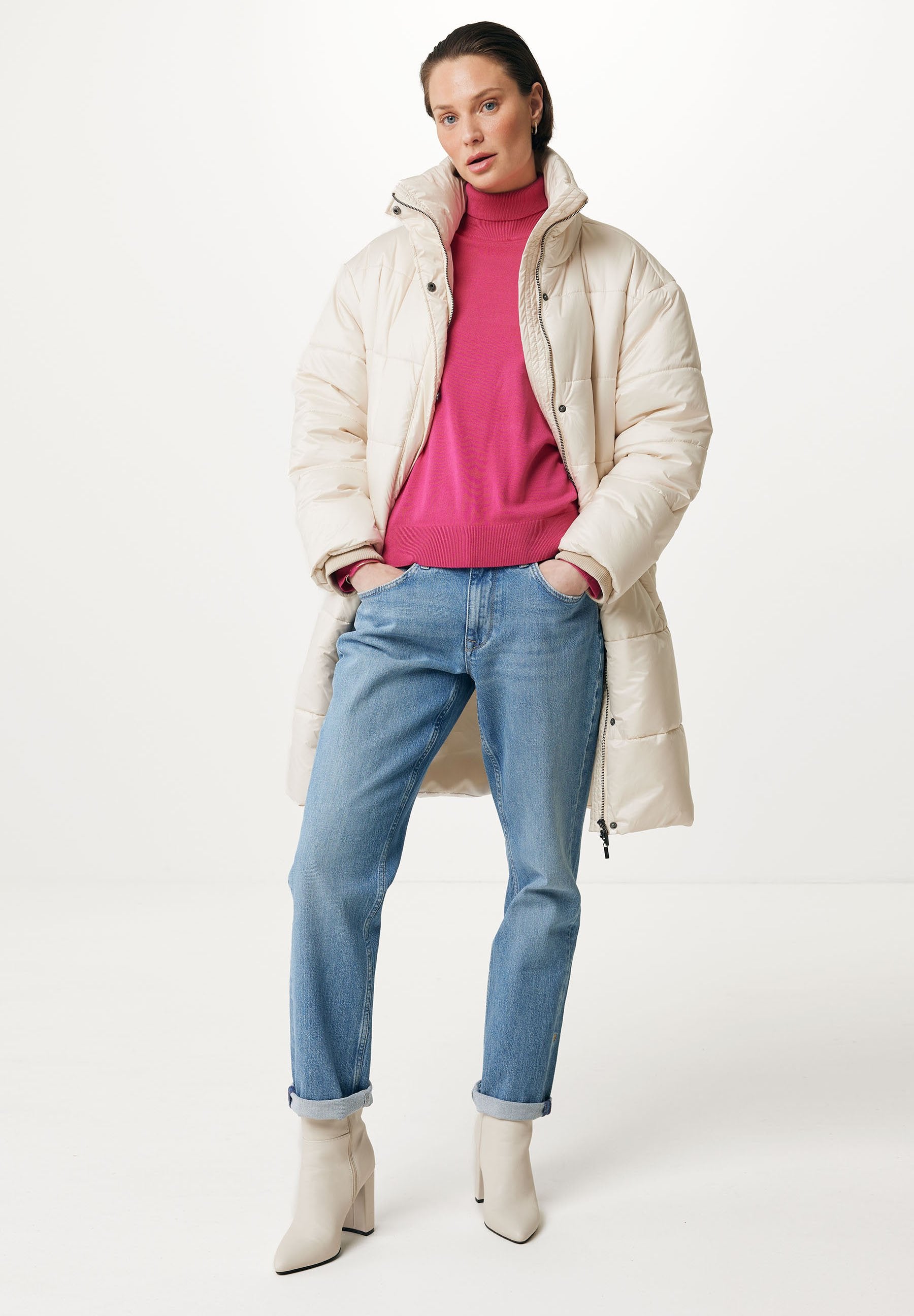 Beige Daunenjacke mit hohem Kragen, über einem knallpinken Rollkragenpullover getragen. Dazu passen hellblaue Straight-Leg-Jeans und cremefarbene Stiefeletten.
