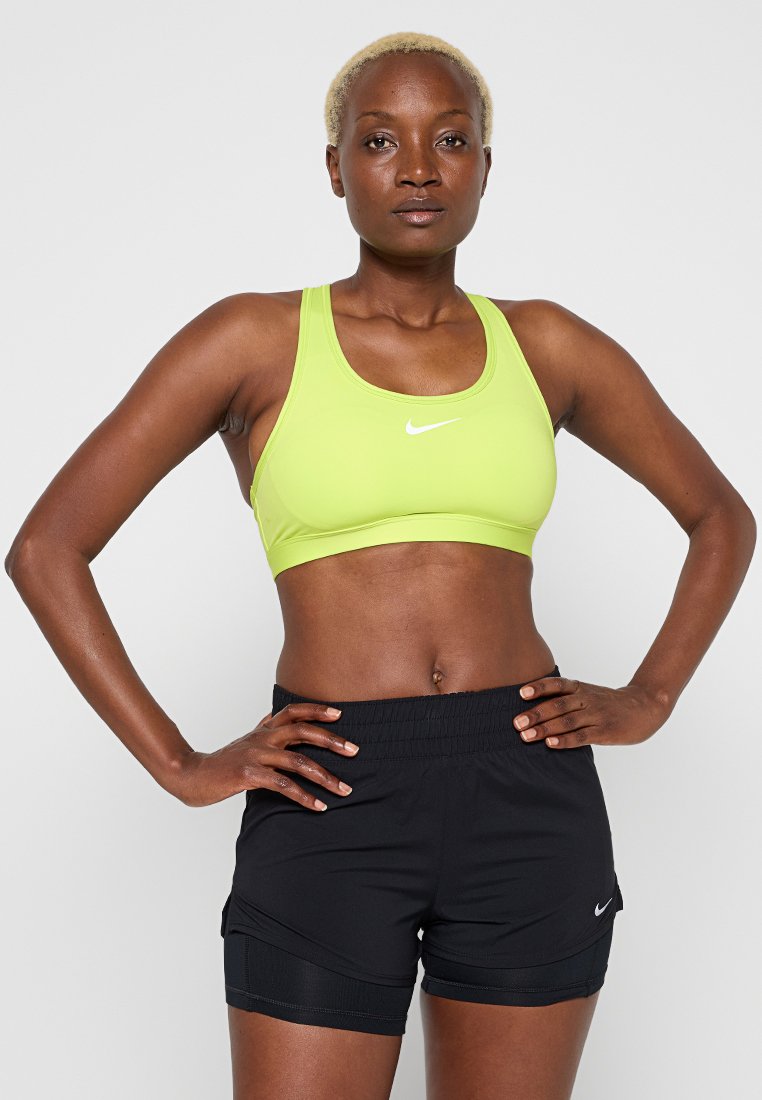 Grüner sportlicher Sport-BH mit rundem Ausschnitt und Logo, kombiniert mit schwarzen Shorts mit Seitentaschen und flexiblem Bund.